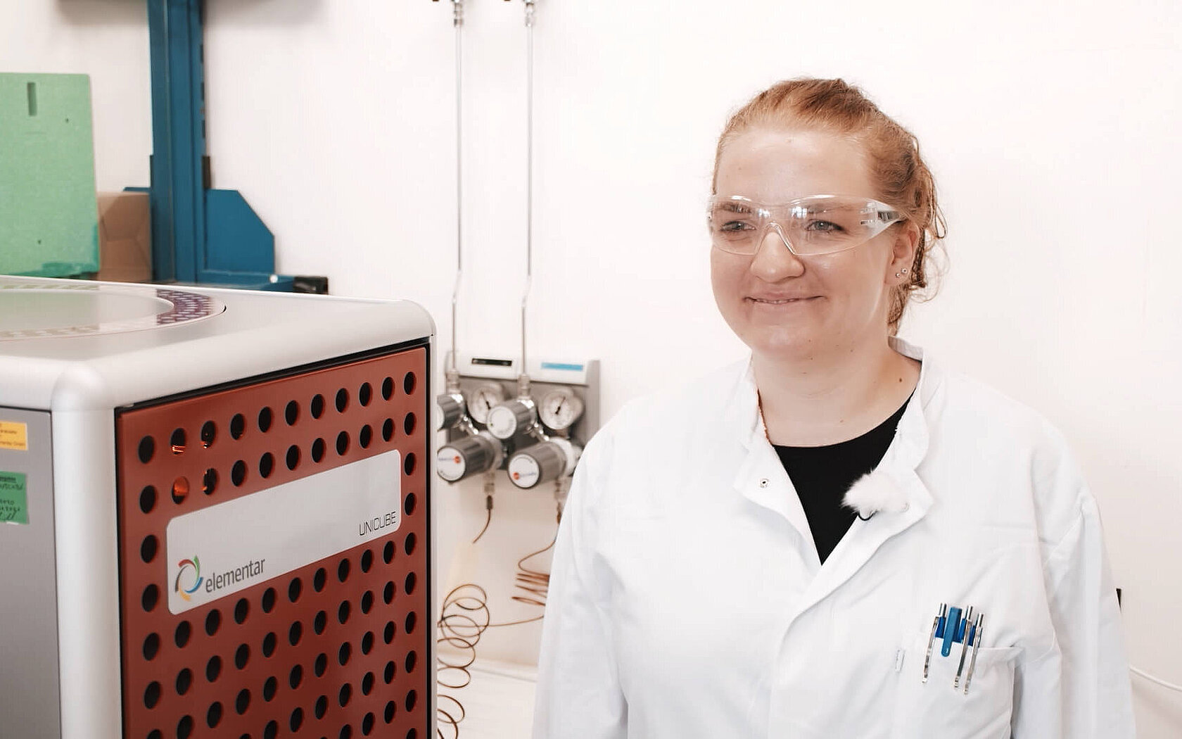 Eine Labormitarbeiterin steht neben einem Elementaranalysator für die Nettopeptidbestimmung