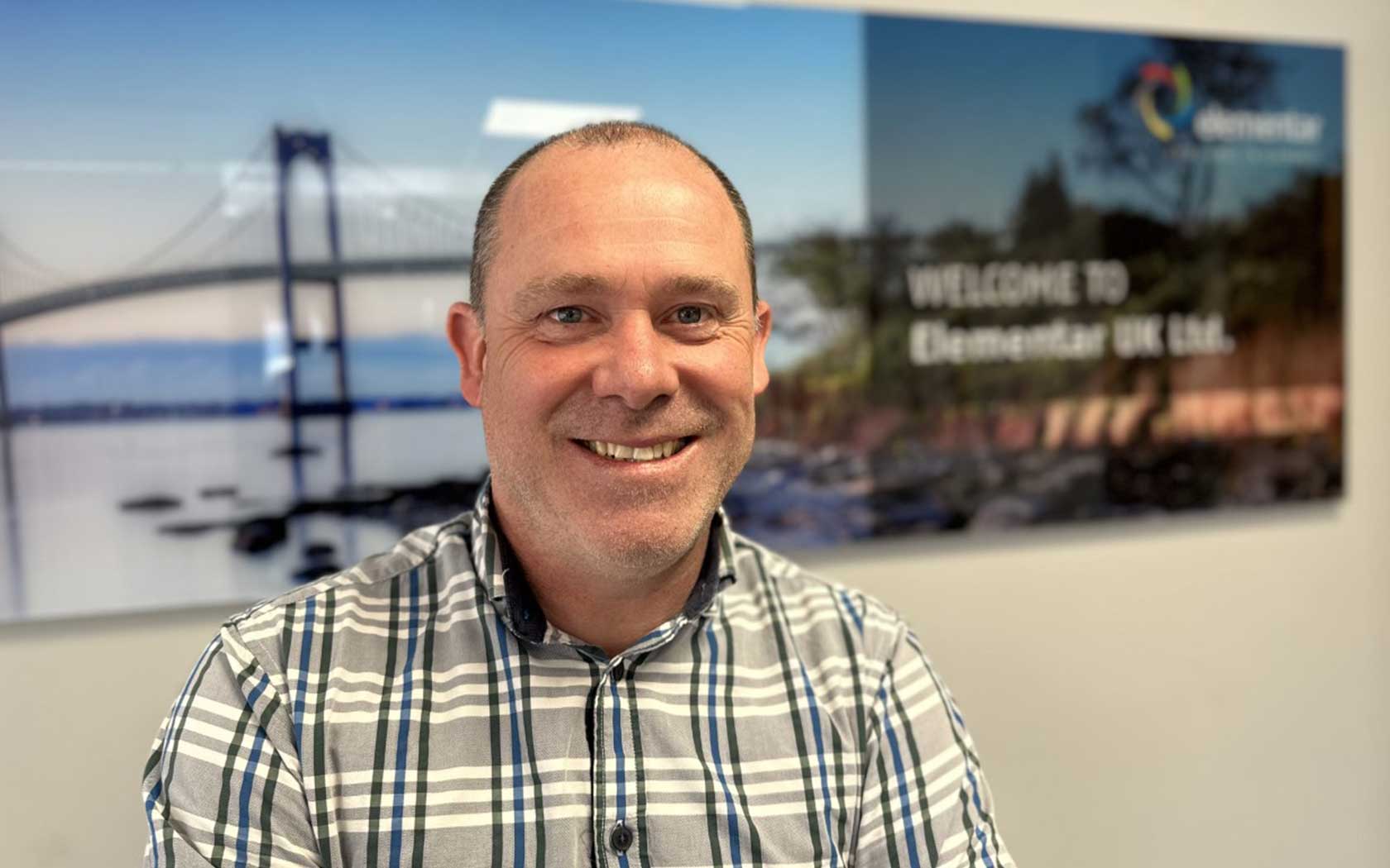 Headshot of a man, sitting in front of a backwall picture